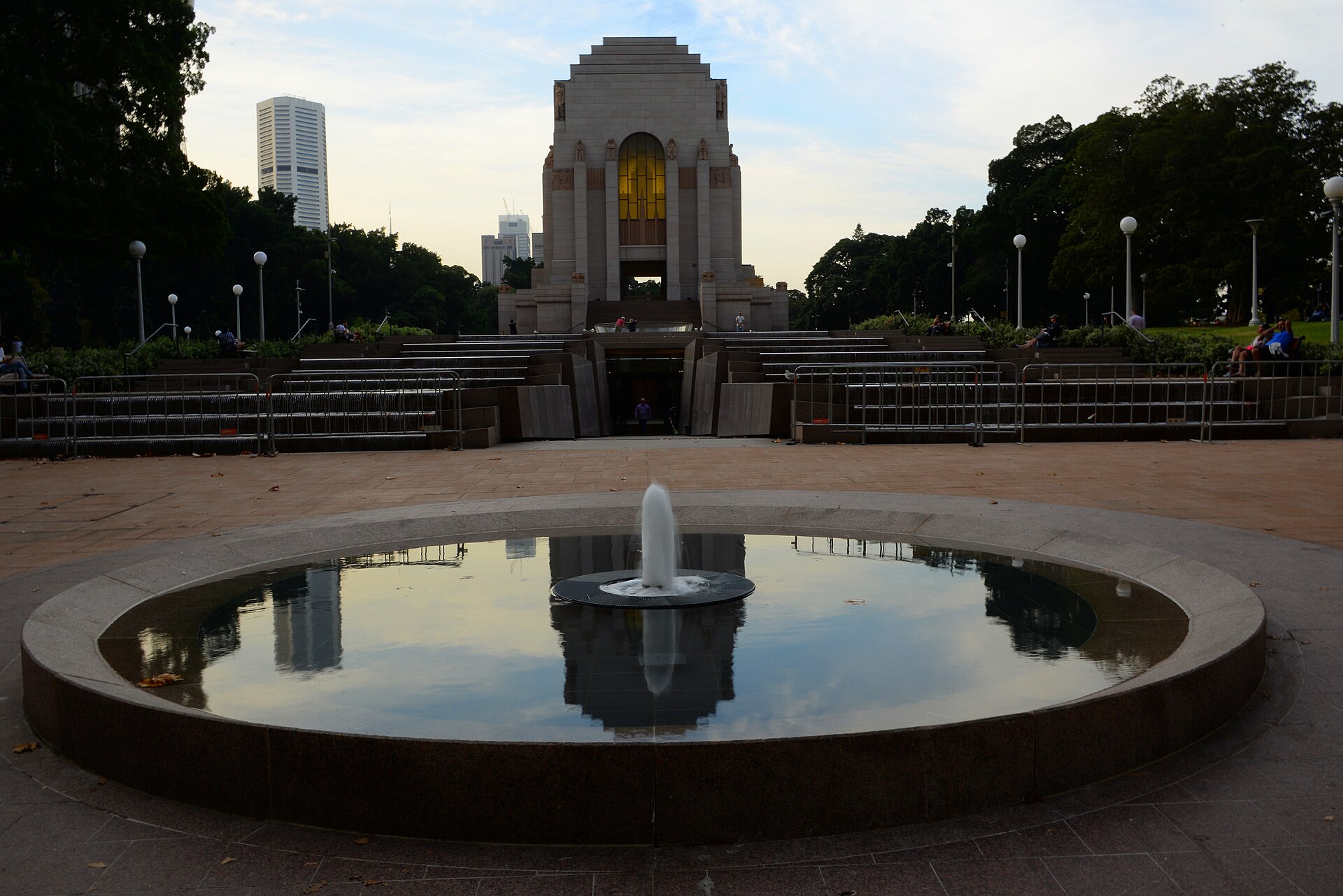 The Art Deco Anzac Memorial in Hyde Park at dusk, with a fountain in a round pool in the foreground and city towers behind