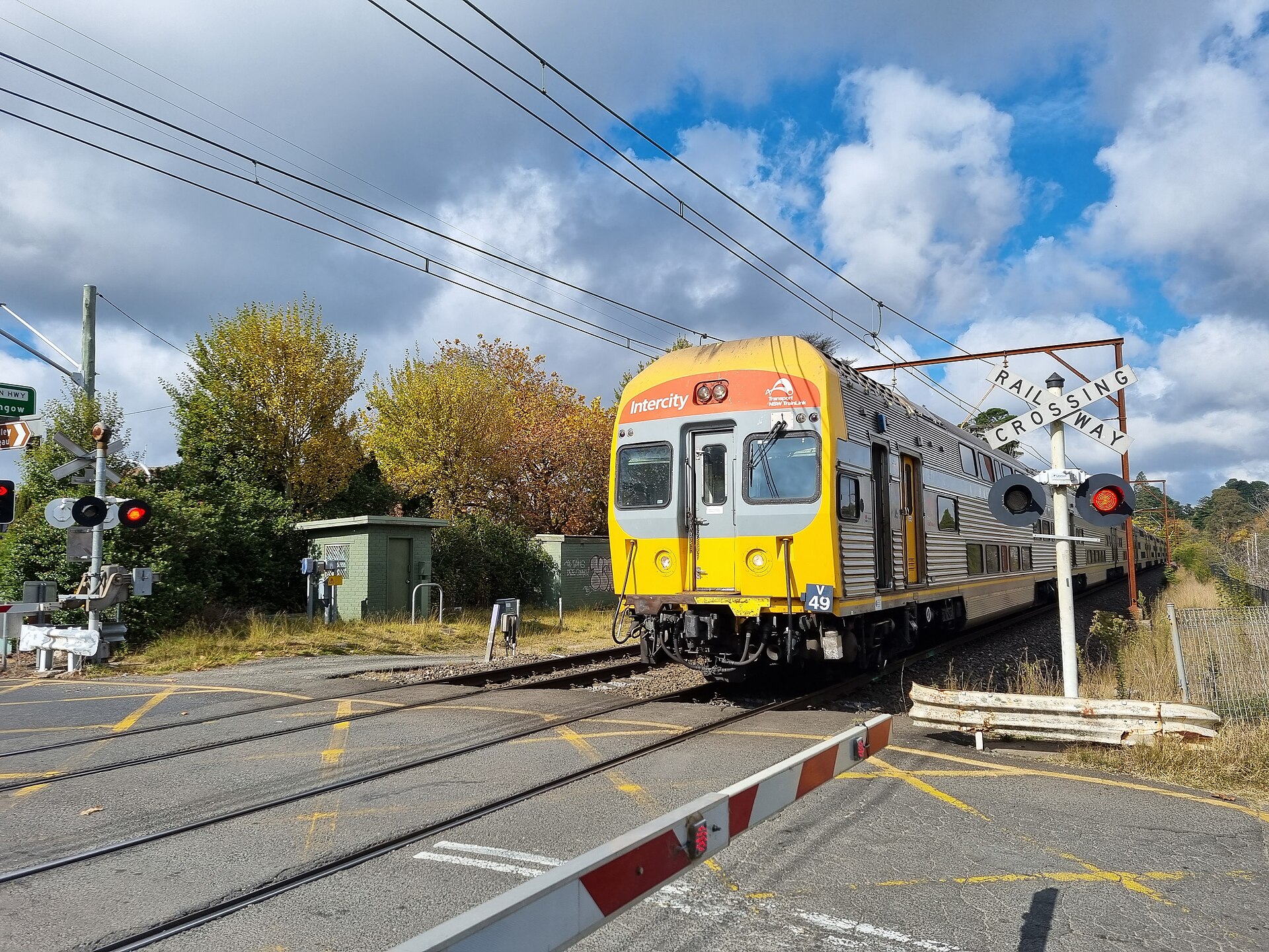 A double-deck Intercity train passing the level crossing beside Blackheath station under autumn trees