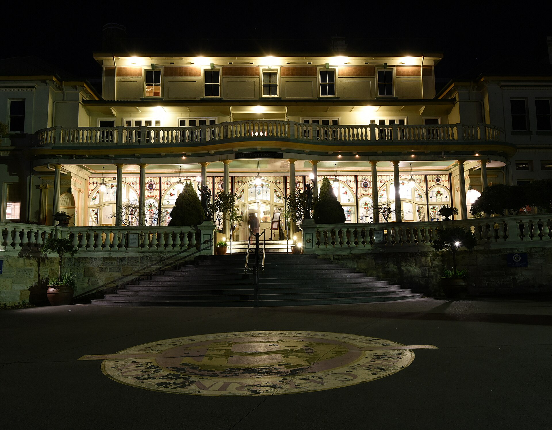 The Carrington Hotel in Katoomba lit up at night, with its curved balcony, columns and stained-glass windows above a wide flight of steps