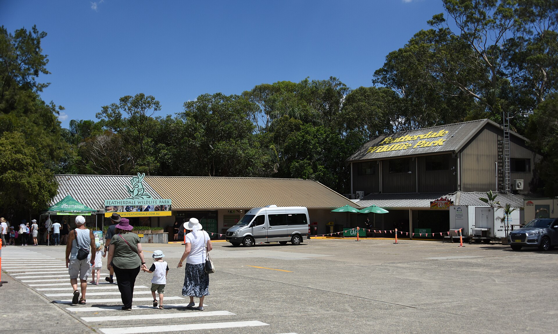 Visitors crossing the car park towards the entrance of Featherdale Wildlife Park with a silver tour minibus parked outside
