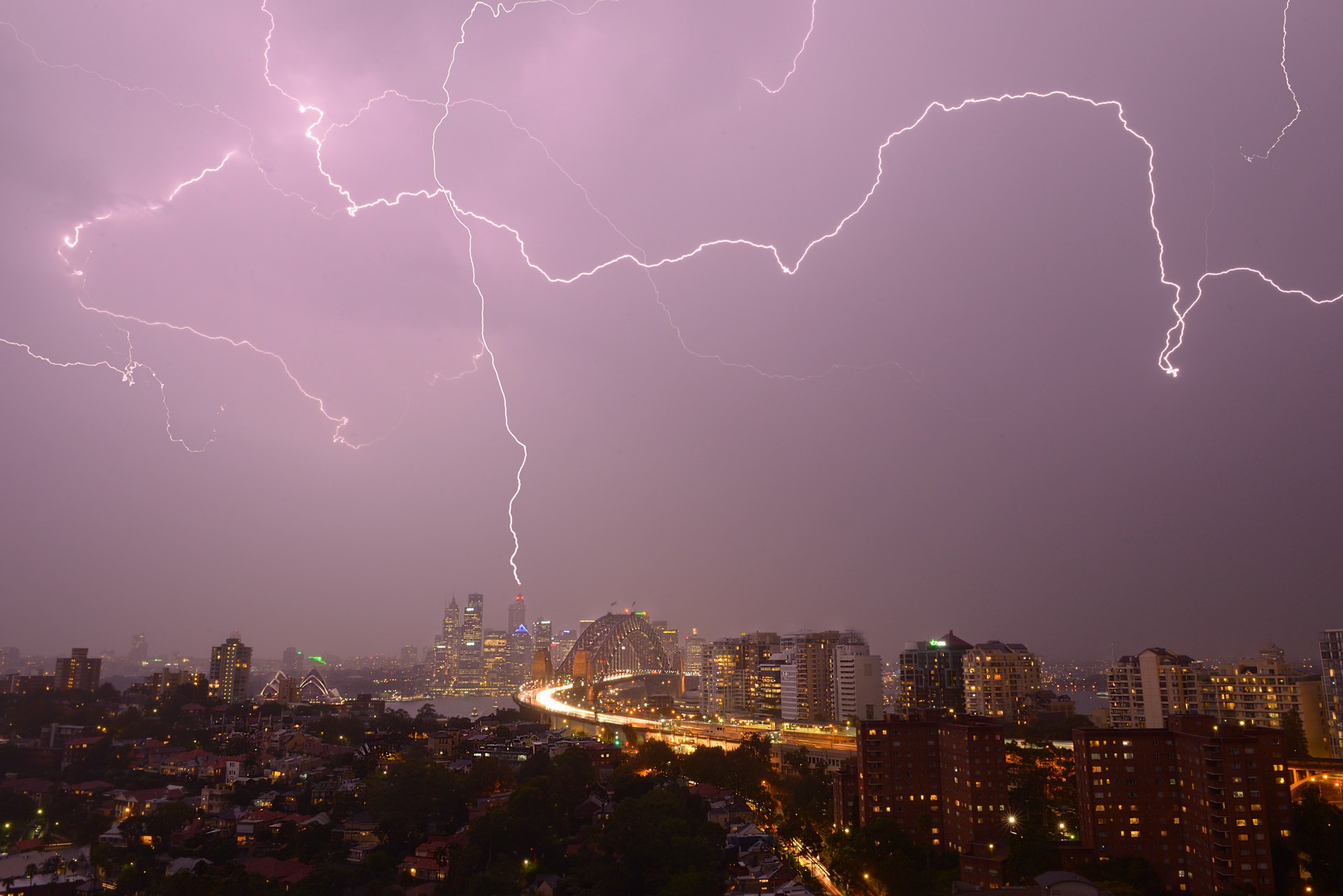 Forks of lightning across a purple night sky above the Sydney CBD, the Harbour Bridge and the Opera House, seen from high above North Sydney