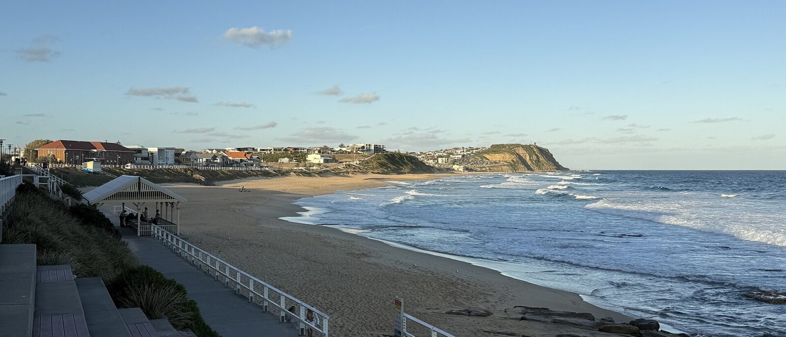 Merewether Beach in Newcastle in late-afternoon light, with a promenade and picnic shelter in the foreground and the coast running north to a headland