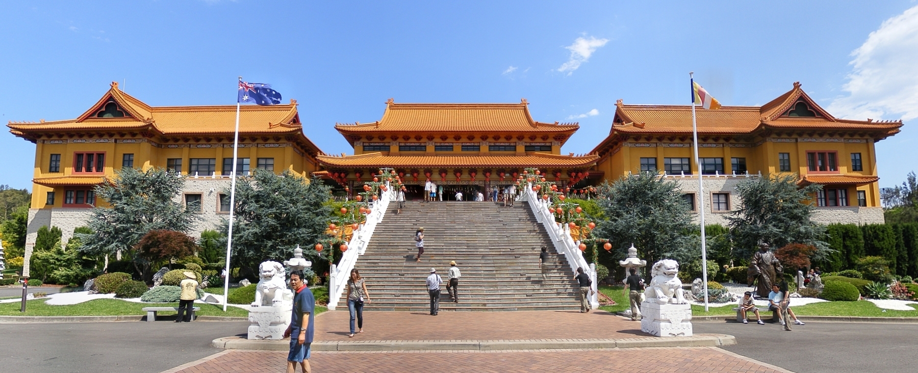 The front of Nan Tien Temple, with ochre-roofed halls on either side of a broad stone staircase flanked by white guardian lion statues and red lanterns