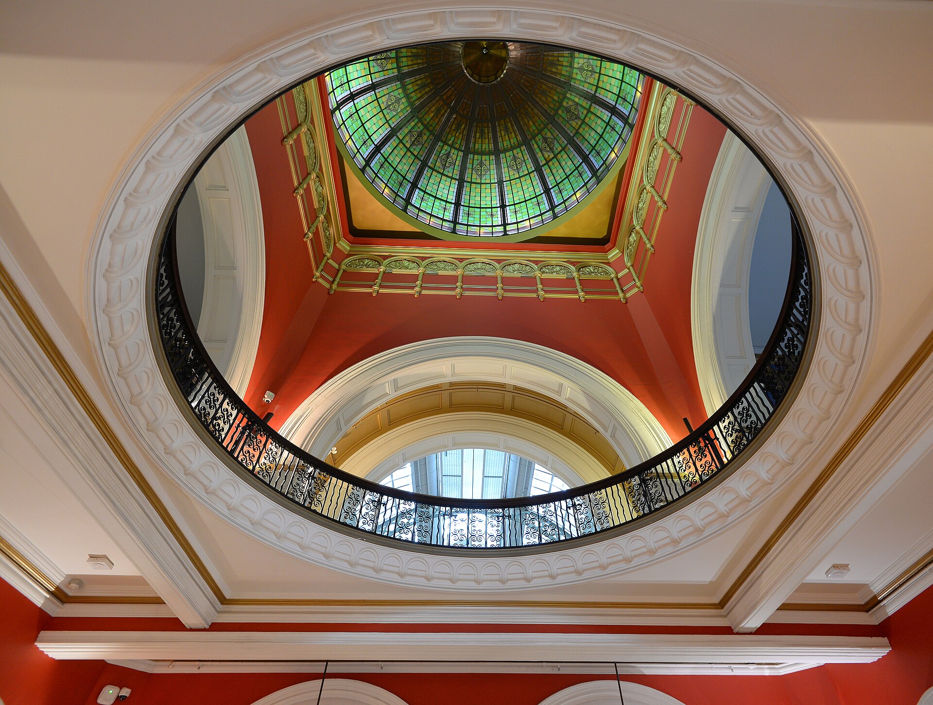 Looking up into the QVB's central dome, with a green and gold stained-glass ceiling, deep red walls, white plasterwork and a circular wrought-iron balcony