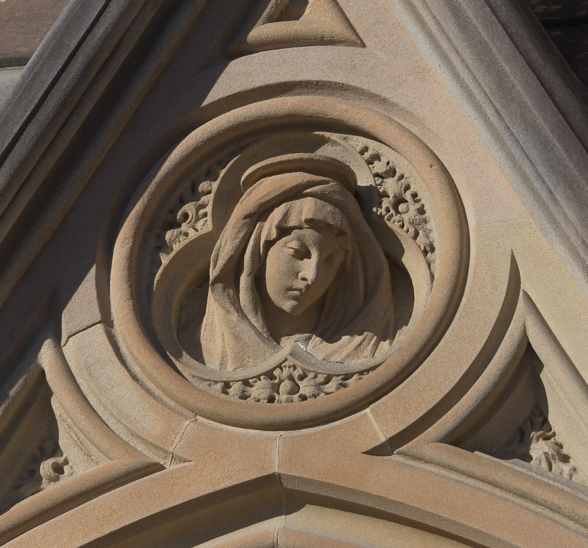 A carved sandstone roundel of the Virgin Mary, her veiled head bowed, set into a triangular gable on the outside of the cathedral