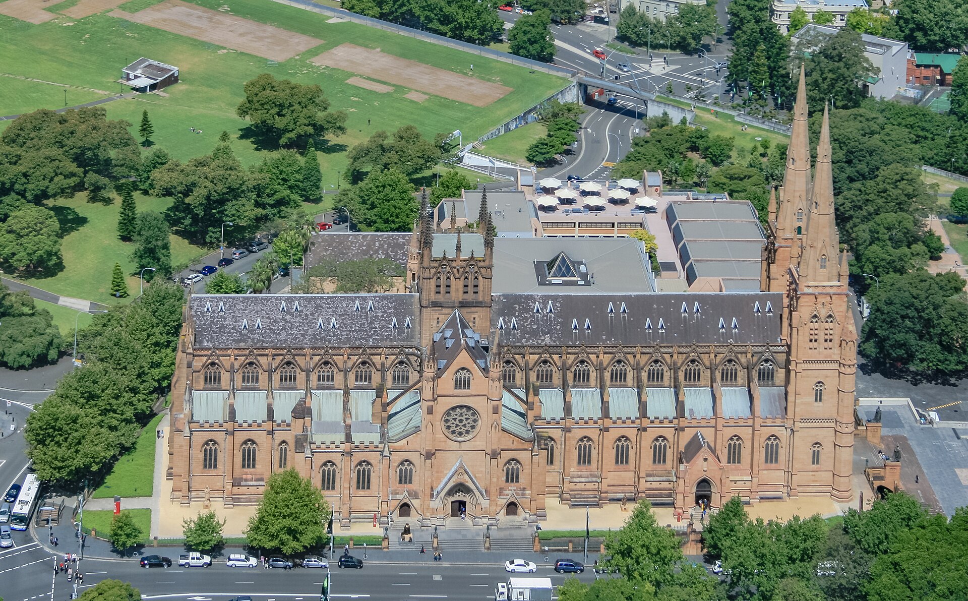 St Mary's Cathedral seen from above, a long sandstone Gothic church with twin spires and a rose window, surrounded by trees and parkland