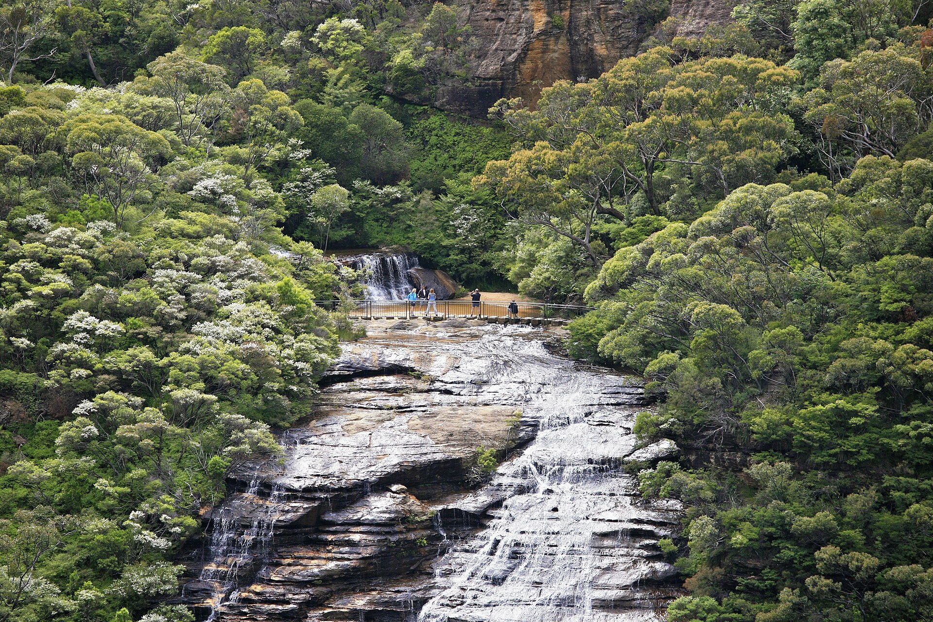 Water pouring over the upper stage of Wentworth Falls with walkers on the viewing platform at the middle crossing
